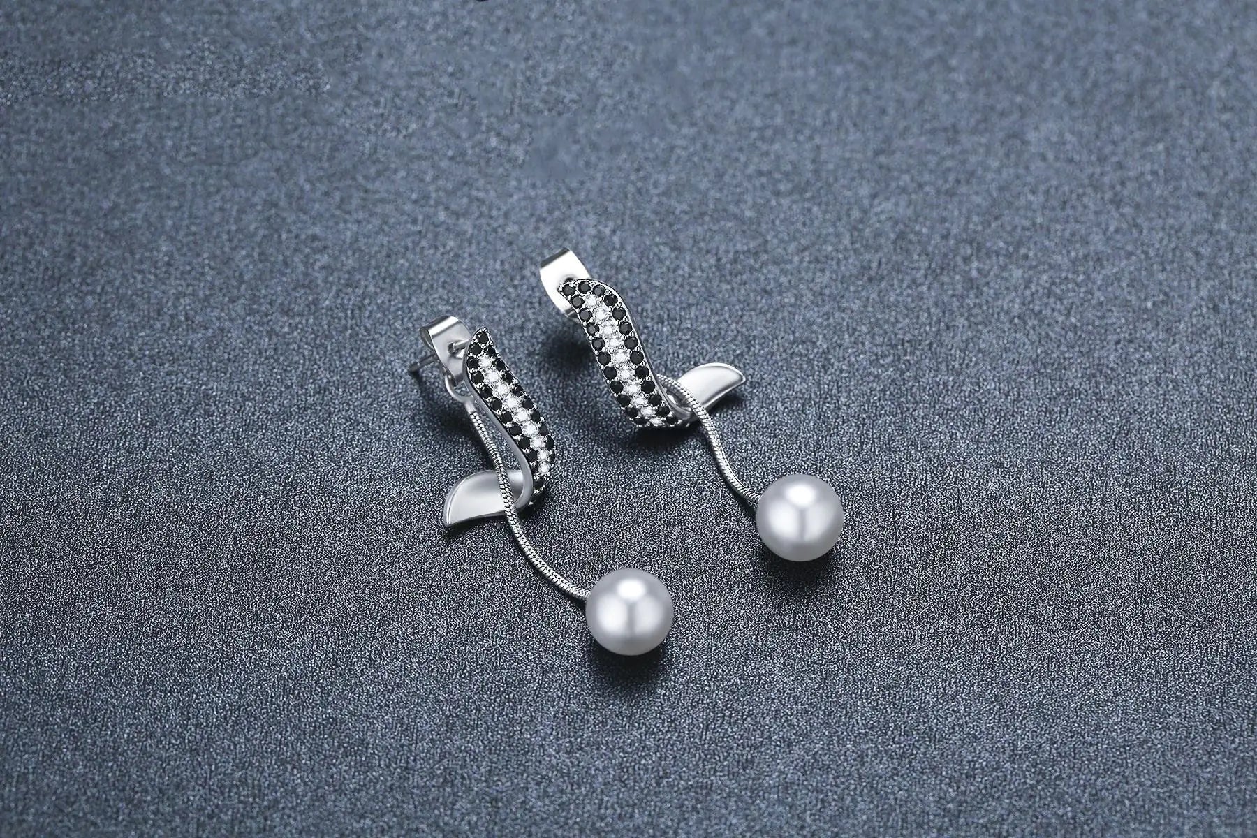 Elegant women's pearl pendant tassel earrings with black accents and silver detailing, displayed on a textured dark background.