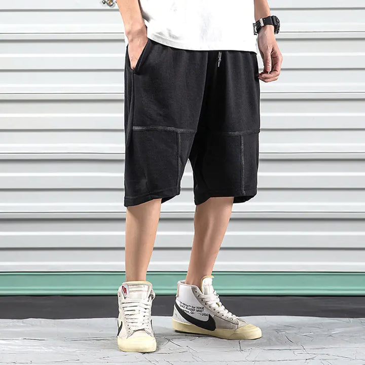 Black Hip-Hop Sports Shorts for Men with relaxed fit and visible seam details, styled with white high-top sneakers.